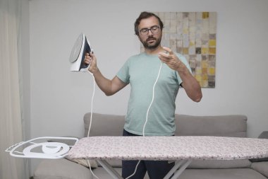 Adam evde giysileri ütülüyor. Çamaşır yıkamak için ütü tahtası kullanan biri. Birlikte ev işi yapan bir çift. Ev temizliği, ev işleri ve günlük rutin işler kavramı.