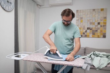 Adam evde giysileri ütülüyor. Çamaşır yıkamak için ütü tahtası kullanan biri. Birlikte ev işi yapan bir çift. Ev temizliği, ev işleri ve günlük rutin işler kavramı.