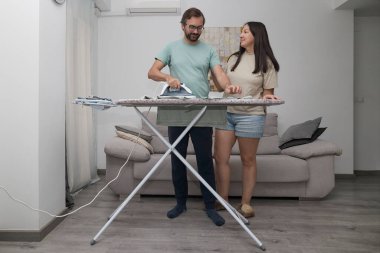 Adam evde giysileri ütülüyor. Çamaşır yıkamak için ütü tahtası kullanan biri. Birlikte ev işi yapan bir çift. Ev temizliği, ev işleri ve günlük rutin işler kavramı.