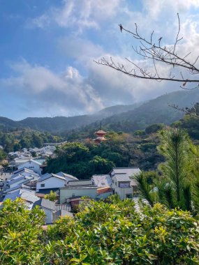 Miyajima Adası 'ndaki sık ormanın üzerinde yükselen kırmızı pagoda. Arka planda mavi gökyüzü var..
