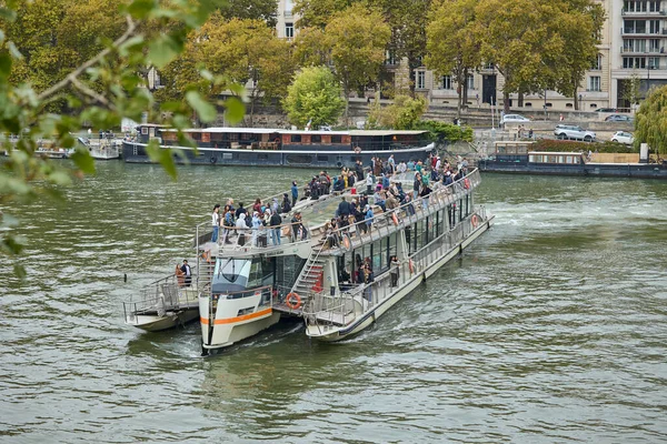 Fransa 'nın Paris kentindeki Seine Nehri boyunca sonbahar ağaçları ve yüzen evlerle çevrili bir tekne dolusu yolcu. Fransız tutsağında popüler bir gezi deneyimi. Paris, Fransa - 10 Ekim 2025.