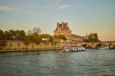 Louvre Müzesi 'nin ve Paris' teki Seine Nehri 'nin yanından geçen turist botuyla günbatımı manzarası. Paris, Fransa - 11 Ekim 2025.