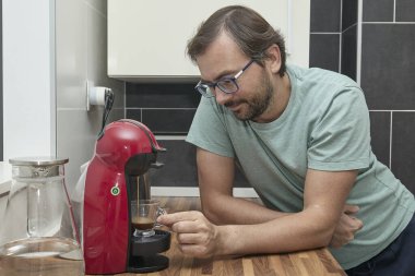 Modern mutfakta kahve makinesiyle kahve yapan adam. Evde espresso hazırlayan ve bir fincan taze kahvenin tadını çıkaran biri. Sabah rutini, ev konforu ve kafein enerjisi kavramı