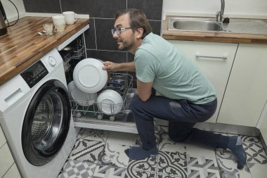 Modern mutfakta bulaşık makinesini yükleyen adam. Ev işleri yapan, bulaşık yıkayan ve evde mutfak gereçleri düzenleyen biri. Ev hayatı kavramı, ev temizliği ve modern yaşam tarzı..
