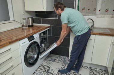 Modern mutfakta bulaşık makinesini yükleyen adam. Ev işleri yapan, bulaşık yıkayan ve evde mutfak gereçleri düzenleyen biri. Ev hayatı kavramı, ev temizliği ve modern yaşam tarzı..