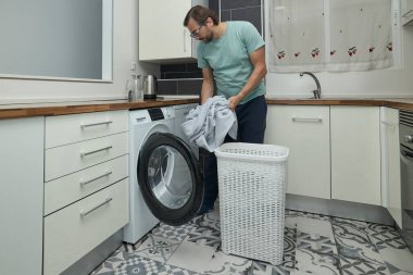 Modern mutfakta çamaşır yıkayan bir adam. Çamaşır makinesini yükleyen ve deterjan dolduran kişi. Ev işleri, ev hayatı ve ev temizliği kavramı