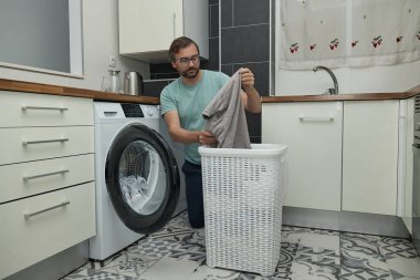 Modern mutfakta çamaşır yıkayan bir adam. Çamaşır makinesini yükleyen ve deterjan dolduran kişi. Ev işleri, ev hayatı ve ev temizliği kavramı