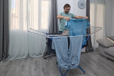 Kadın ve erkek çamaşırlarını evde kurutuyorlar. Kurutma askısına asılan ve temiz giysiler katlanan bir çift. Ev işleri, ev işleri ve günlük rutin işler kavramı.