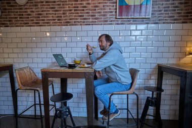 Adam kafede dizüstü bilgisayarla çalışırken tatlı yiyor..