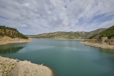 Sakin turkuaz rezervuar kayalık tepeler ve bulutlu gökyüzünün altındaki yeşil yamaçlarla çevrili. İspanya 'da huzurlu doğal ortam.