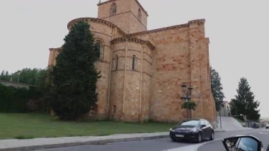 Avila İspanya 'da bir ortaçağ taşından kilisenin virajlı bir caddeden geçen bir arabasının sinematik bir çekimi..