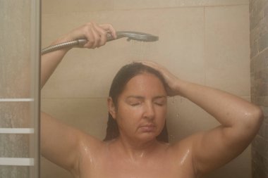 Saçlarını su altında yıkarken duş alan bir kadın. Buharlı bir banyoda rahatlama ve hijyen..