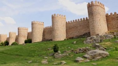 Avila İspanya 'nın ikonik ortaçağ şehir duvarlarının panoramik görüntüsü. Parlak bir gökyüzü altında devasa taş kuleler ve siperler var. Seyahat içeriği için mükemmel tarihi belgeseller mimari çalışmaları ve turizm reklamları.