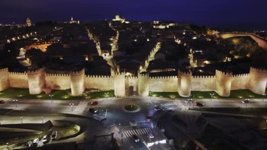 Avila 'nın eski caddelerinin üzerindeki hava manzarası gece yarısı devasa ortaçağ duvarlarının arkasında tarihi şehir planlarını ve sıcak şehir ışıklarını gösteriyor..