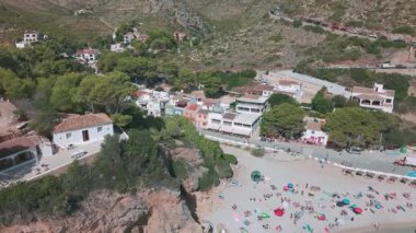 Cala Granadella kumsalının renkli şemsiyeleri, beyaz evleri ve turkuaz Akdeniz suları yakınında dinlenen turistlerin insansız hava aracı görüntüleri. Javea, İspanya - 4 Ekim 2025.