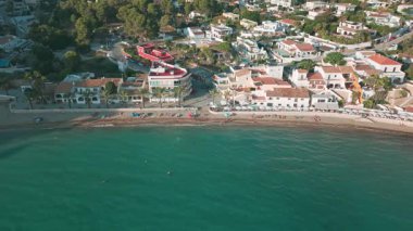 İspanya 'da Moraira sahilinin insansız hava aracı görüntüsü. İnsanlar dinleniyor, şemsiyeler, palmiye ağaçları ve Akdeniz kıyısındaki kıyı evleri..