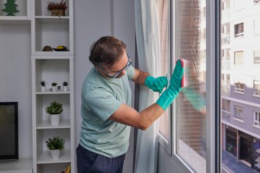 Evdeki pencereleri sünger ve spreyle temizleyen adam..