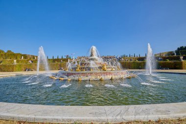 Arka planda güçlü su jetleri ve Versailles Sarayı olan büyük bir çeşmenin manzarası, ikonik Fransız simgesi. Versailles, Fransa - 12 Ekim 2025.
