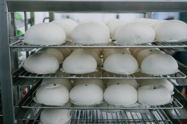 Ticari bir mutfakta veya gıda üretim tesisinde paslanmaz çelik soğutma raflarına yerleştirilmiş taze pişmiş beyaz çörekler..