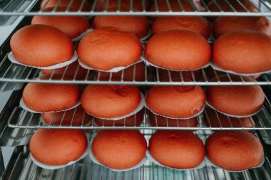 Ticari bir mutfakta veya gıda üretim tesisinde paslanmaz çelik soğutma raflarına yerleştirilmiş taze pişmiş kırmızı çörekler..