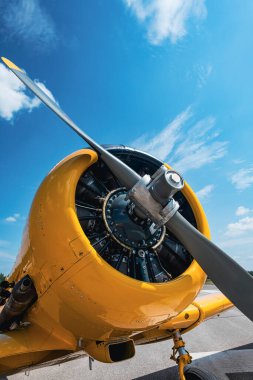 Düşük açılı sarı askeri eğitim uçağı radyal motoru ve pistteki gümüş pervane. Ön çeyrekte ayrıntılı motor silindirleri, kaplama, iniş takımları ve egzoz gösteriliyor. Yerden parlak mavi gökyüzüne karşı.