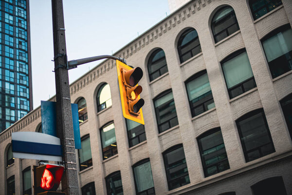 Вид спереди желтого светофора, висящего на столбе при естественном освещении, снятый на уровне улицы широкоугольным объективом. Центральные здания формируют фон. Горизонтальное фото.