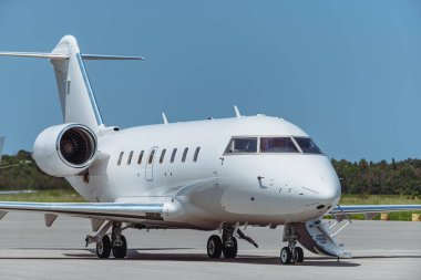 Havaalanı pistine park etmiş beyaz çift motorlu jet uçaklarının yan görüntüsü. Kokpit pencerelerini, gövde pencerelerini, kuyruk kanatlarını, iniş takımlarını gösteren uçaklar. Yeşil orman ve mavi gökyüzü arka planda görünür..