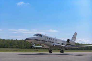 Küçük bir jet küçük bir bölgesel havaalanının pistinden havalanır. Tekerlekler yerden ayrıldı ve uçak inmeye başladı. Açık mavi gökyüzü çerçevenin çoğunu doldurur.