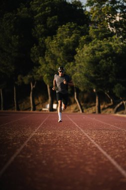 Arka planda ağaçlarla koşu pistinde erkek atlet eğitimi