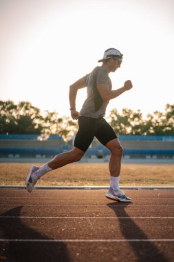 Erkek sporcu spor yaparken fiziksel olarak antrenman ve koşu pistinde koşuyor.