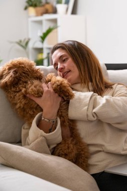 Evdeki kanepede rahat bir şekilde otururken kaniş köpeğiyle oynayan bir kadın.