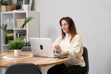 Uzaktan kumanda için dizüstü bilgisayar kullanan bir kadın, rahat ev ofisinde bağlı ve üretken kalıyor.