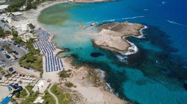 Gün batımında deniz kenarı, kayalık kıyılar ve sakin okyanusun yer aldığı manzaralı bir sahil şeridinin yüksek kaliteli hava fotoğrafı. Denize yansıyan altın saat ışığı, barışçıl ve atmosferik bir kıyı manzarası yaratır. Seyahat ve yaz tatili için ideal.