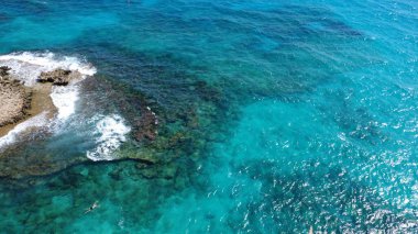 Gün batımında kayalık kıyı şeridi ve sakin denizi olan bir kıyı kasabasının yüksek kaliteli hava fotoğrafı. Güneş ışığı, okyanus suyunu, deniz kenarındaki binaları ve temiz gökyüzü altındaki manzaralı kıyı manzarasını yansıtıyor. Seyahat, turizm, tatil, yaz için ideal.