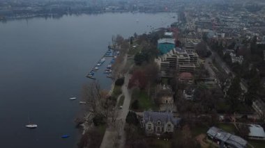 Sakin bir gölün şehir limanı ve konut binalarıyla çevrili pürüzsüz hava görüntüleri. Limanda demirli tekneler, şehir parkı ve bulutlu bir günde yukarıdan çekilen sessiz caddeler. İş sunumları, emlak ve turizm için ideal