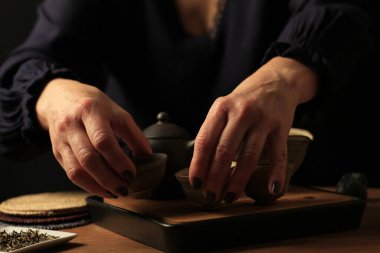 Sıcak ışıkta seramik çaydanlık, fincanlar ve ahşap bir masada gevşek yaprak çayıyla samimi çay seremonisi sahnesi. Yavaş yaşam, farkındalık, konfor, ev ritüelleri ve çay kültürü kavramlarına uygundur..