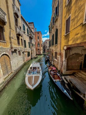 Klasik bir gondol ve modern bir su taksisini (motoscafo) Venedik, İtalya 'daki dar ve eski bir kanalda çekerek çekilen parlak, yüksek açılı bir çekim. Görüntü tarihi mimariyi vurguluyor, eski binaların altın renklerini.,