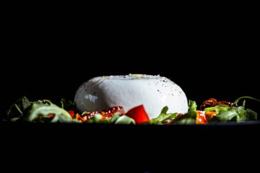 Fresh burrata cheese served on a bed of arugula, ripe tomatoes, and dried tomatoes on a dark background