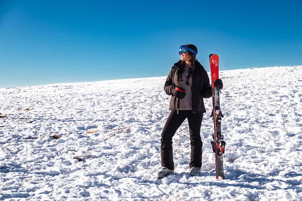 Karlı bir dağda elinde kayaklarla duran genç bir kadın kış sporlarının tadını çıkarıyor.
