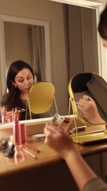 Göz kalemi ve göz farı süren güzel bir kadın gösterişli aynanın önünde sıcak bir ışık ile.