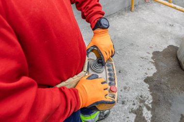 İşçi inşaat sırasında uzaktan kumanda kullanıyor, güvenlik eldiveni takıyor.