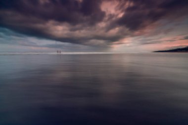 Kuta Beach, Bali 'de insan siluetiyle dramatik Gündoğumu Yansımaları