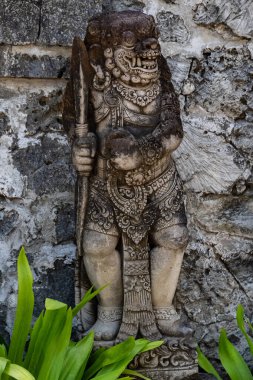 Yeşillik bir tropikal Bali bahçesine yerleştirilmiş süslü taş heykeller. Ayrıntılı heykellerde, seyahat, miras ve mimari temalar için ideal huzurlu ve kültürel bir atmosfer yaratan geleneksel Balili sanatsal motifler yer alıyor..