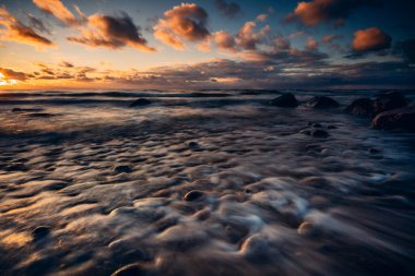 Kayalık bir sahilde, Litvanya 'da dalgaların üzerinde kasvetli bir gün batımı 