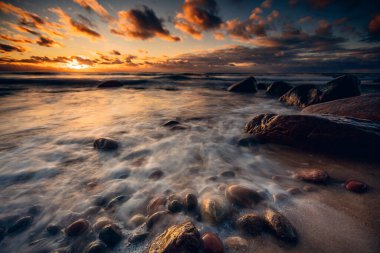 Kayalık bir sahilde, Litvanya 'da dalgaların üzerinde kasvetli bir gün batımı 