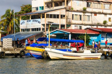 Renkli tekneler Livingston, Guatemala 'daki Karayipler rıhtımına yanaştı. Tropikal palmiye ağaçları, canlı binalar ve dramatik bulutlar canlı bir sahil atmosferi yaratıyor..