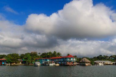 Colorful boats docked along the Caribbean waterfront in Livingston, Guatemala, with tropical palm trees, vibrant buildings, and dramatic clouds creating a lively coastal atmosphere.