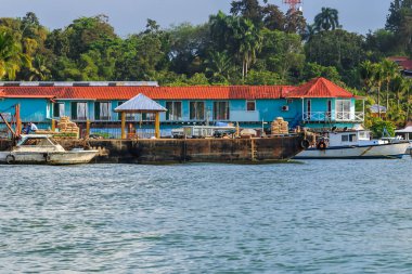 Renkli tekneler Livingston, Guatemala 'daki Karayipler rıhtımına yanaştı. Tropikal palmiye ağaçları, canlı binalar ve dramatik bulutlar canlı bir sahil atmosferi yaratıyor..