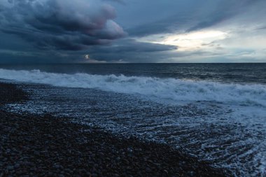 Atlantik dalgaları alacakaranlıkta karanlık bir çakıl taşı plajına çarptığında Madeira 'nın engebeli volkanik kıyı şeridinde dramatik fırtına bulutları toplanıyor..