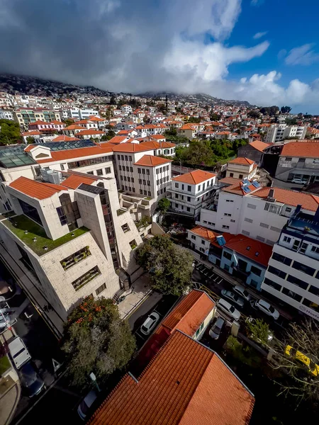 Funchal, Madeira 'nın panoramik manzarası, yumuşak sis ve bulutlar altında yemyeşil tepelere yayılmış kırmızı kiremitli çatıları olan renkli evler sergiliyor..